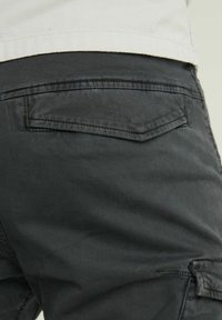 Dunkelgraue Cargo-Shorts mit glatter Textur, ausgestattet mit einer Gesäßtasche mit rechteckigem Klappenverschluss und kontrastierenden Nähten.