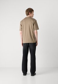 Tricou cu mânecă scurtă, de culoare maronie, confecționat dintr-un material moale, asortat cu blugi negri cu croială lejeră. Designul este simplu, cu o croială dreaptă și detalii minime.