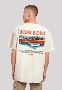 Cream-colored short-sleeve t-shirt featuring a colorful graphic print of waves and text: "BORA BORA Leeward Islands" on the back.
