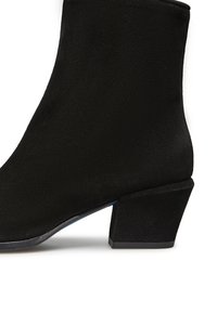 Stivale alla caviglia in suede nero con un design elegante, tacco quadrato e superficie liscia. Presenta un bordo superiore leggermente curvato per un tocco di dettaglio in più.