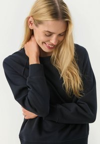 Námornícky modrá mikina z měkké tkaniny s pružnými manžetami a výstřihem. Má volný střih a jemné šití na rukávech.