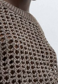 Pull marron en maille avec un motif en maille ouverte, col rond et bordures côtelées. La texture est légère et respirante.