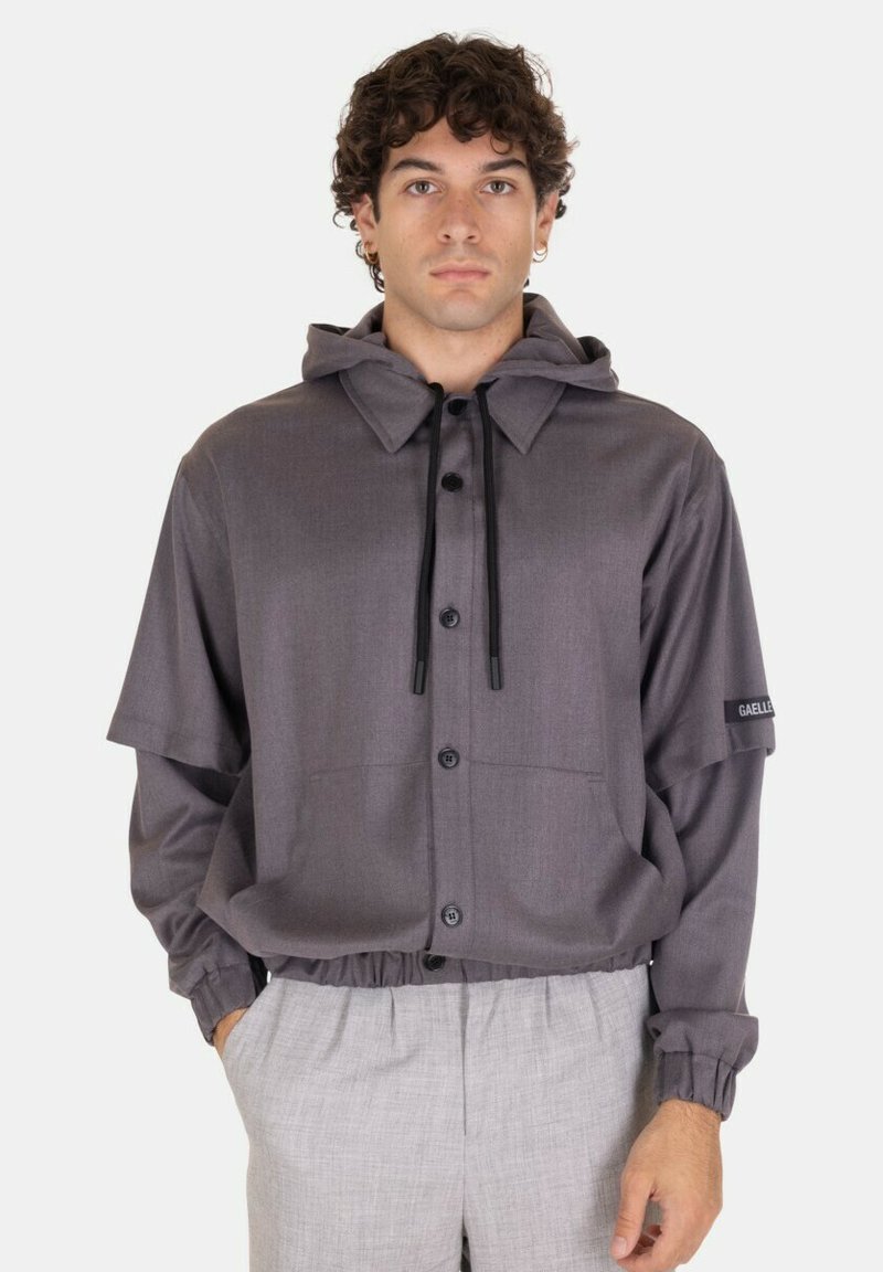 Giacca grigia con cappuccio, dal taglio comodo, con bottoni a pressione, polsini elasticizzati e un accento del logo sulla manica. Tessuto dalla texture morbida, design contemporaneo.