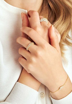 Guldsmycken med ädelstensdetaljer. Inkluderar två ringar med vågformad design och ett fint armband med ett centralt gnistrande inslag.