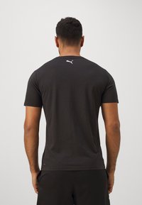 Camiseta preta de manga curta em algodão, com gola redonda e um pequeno logótipo branco nas costas. Textura suave e design ajustado.