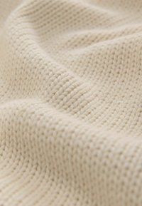 Helles beige gestricktes Gewebe mit einer strukturierten Oberfläche, das ein enges Maschenmuster aufweist. Weich und flexibel mit einem glatten, natürlichen Gefühl.