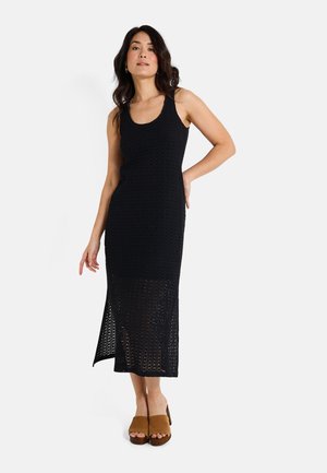 Vestido de tirantes de ganchillo negro con un cuerpo ajustado, abertura hasta la rodilla y un patrón texturizado. Combinado con sandalias de plataforma marrón.