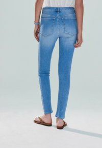 Vaaleansiniset slim fit -farkut, joissa on kulutettu ilme, kaksi takataskua ja sileä pinta, yhdistettynä ruskeisiin flip-flop -sandaaleihin.