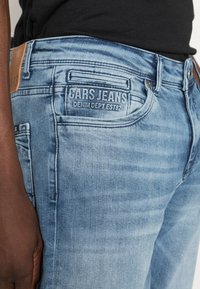 Lichtblauwe denim jeans met een vervaagde afwerking, voorzien van een leren logo patch en gedetailleerd stiksel. Het achterzak toont de "CARS JEANS" branding.