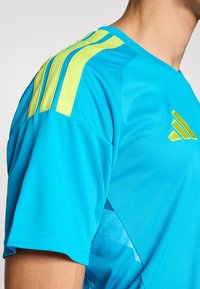 Ανοιχτό μπλε αθλητικό πουκάμισο με κίτρινες ρίγες στους ώμους, με ομαλή υφή και διακριτικό μοτίβο βαθμιαίας αλλαγής χρώματος στο πλάι.