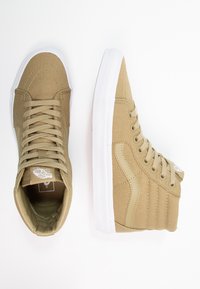 Beige High-Top-Canvas-Sneaker mit weißen Gummisohlen und beigen Schnürsenkeln, von oben und von der Seite auf einem weißen Hintergrund gezeigt.
