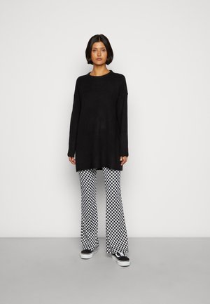 Pull en tricot noir à manches longues, associé à un pantalon à carreaux noir et blanc évasé et des baskets noires. Simple, coupe décontractée.