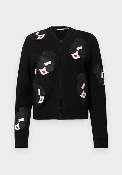 Crni kardigan na patentni zatvarač s aplikacijama lica sa sunčanim naočalama i crvenim usnama, izrađen od mekanog materijala i s rebrastim manžetama.