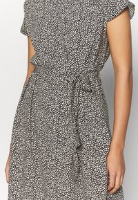 Vestido negro con estampado floral blanco, mangas cortas y un cinturón atado en la cintura. Tejido ligero con un diseño fluido.
