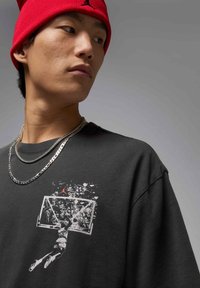 Black cotton t-shirt featuring a graphic of a basketball player dunking, with a red logo and two silver chains worn around the neck.