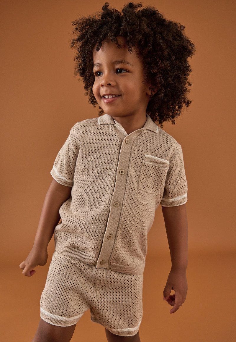 Chemise beige en maille à manches courtes et short assorti avec un motif texturé, dotés d'un col, de boutons et d'une poche poitrine avec des accents côtelés.