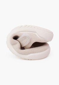 Světlé béžové tenisky s texturovaným pleteným svrškem, zaobleným designem a gumovou podrážkou. Mají měkký slip-on vstup a výrazné švy.