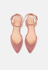 Chaussures plates en daim rose avec bout pointu, brides autour de la cheville et accents de boucles dorées. Intérieur lisse et extérieur texturé.