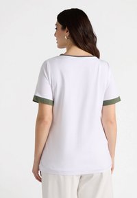 Weißes kurzärmliges Hemd mit grünen Akzenten an den Bündchen, rundem Ausschnitt und glatter Textur, kombiniert mit hellen Hosen.