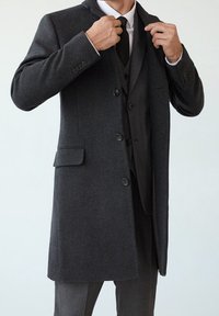 Lang, donkergrijze wollen jas met drie knopen, notch-kraag en zijzakken, gedragen over een zwart vest en stropdas, met een gladde textuur.