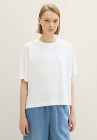T-shirt bianca oversize in cotone, con maniche corte e scollo rotondo, abbinata a un pantalone denim blu largo.