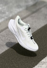 White athletic shoe with a perforated mesh upper, rubber sole, and black toggle lacing. Features a subtle logo on the side and molded heel.