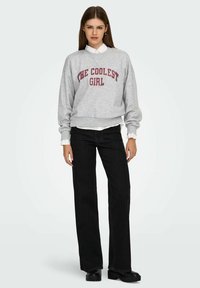 Hall hallipluus "THE COOLEST GIRL" marooniga trükituna, koos mustade laiade pükste ja mustade paksude saapadega. Allosas paistab valge krae.