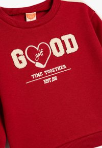 Felpa rossa con colletto a coste, con lettering bianco testurizzato: "GOOD", "golf" e "TIME TOGETHER EST 86" sul davanti.