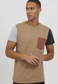 Brun t-skjorte med grå og svarte korte ermer, med en maroon brystlomme og en klassisk rund hals. Myk bomullsblanding.