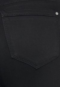 Zwarte denim jeans met een gestikte achterzak in een driehoekige vorm en een kleine metalen accent. Gladde textuur en een strak design.