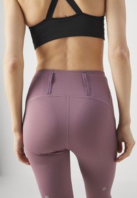 Leggings de cintura alta morados con una textura suave y dos bolsillos traseros. Sujetador deportivo negro con diseño de espalda nadadora.