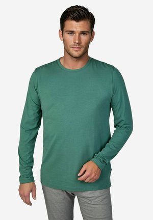 Long-sleeve crewneck shirt in green cotton material with a smooth texture, paired with grey pants. Features a small logo on the chest.