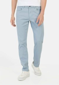 Jasnoniebieskie dżinsy o slim fit, z pięcioma kieszeniami i zapięciem na zamek. Materiał o gładkiej teksturze, zestawione z białymi trampkami.