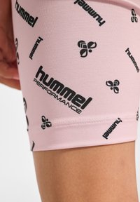 Lichtroze sportshorts van stretchy materiaal, met zwarte "hummel"-logo's en grafische patronen over de gehele stof. Close-up weergave.