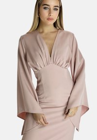 Vestido de manga larga en rosa suave, con escote pronunciado, cintura fruncida y mangas acampanadas con puños abiertos. Textura suave y mate.