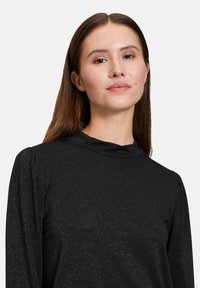 Langärmliges schwarzes Oberteil mit subtiler Glitzertextur, hohem Kragen und Puffärmel-Details für zusätzliche Dimension.