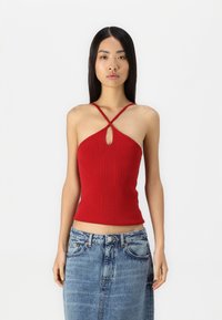 Top de halter de punto acanalado rojo con un detalle de ojal, tirantes delgados entrelazados y un silueta ajustada. Combinado con una falda de mezclilla azul claro.