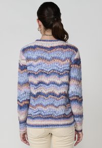 Pull en tricot aux couleurs pastel, présentant des rayures ondulées en bleu, rose et beige. Design texturé en tricot lâche avec un ourlet et des poignets côtelés.