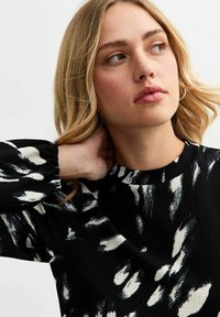 Un pull en tricot à motifs noir et blanc, doté d'un design texturé, d'un col rond et de manches bouffantes avec des poignets élastiques.