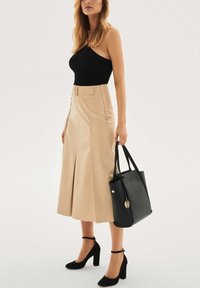 Juodas ribuotas viršus, smėlio spalvos A formos sijonas su priekiu skeltuku ir diržu, juoda klasikinė rankinė ir juodi aukštakulniai su čiurnos dirželiu ir stambiu kulnu.