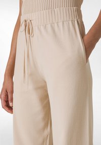 Beige weite Hose aus weichem Stoff, mit einem gerippten elastischen Bund, Kordelzug und seitlichen Taschen.
