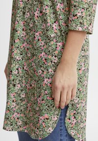 Blumenmuster-Tunika mit grünen, rosa und orangen Mustern, aus leichtem Stoff gefertigt. Verfügt über einen abgerundeten Saum und eine lockere Passform.