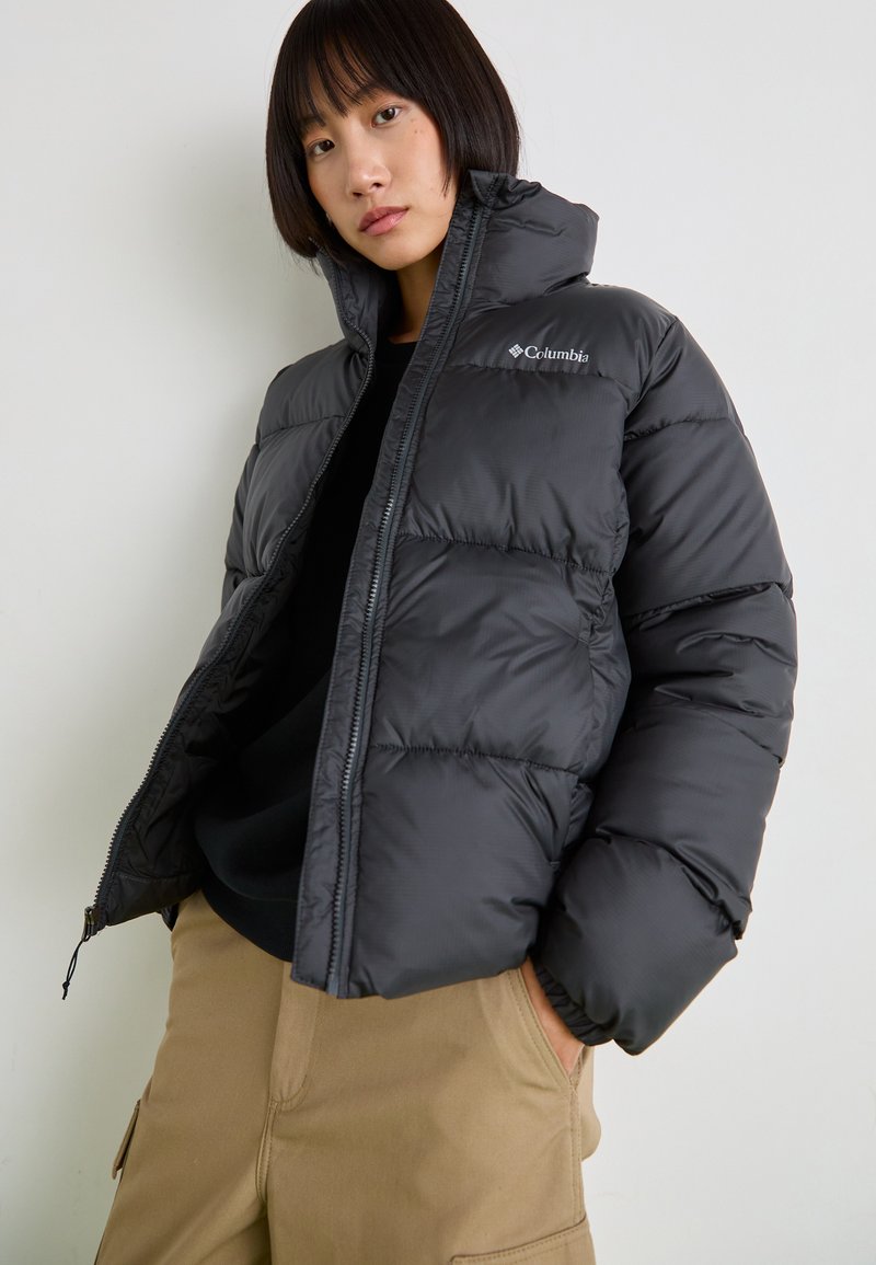 Zwarte puffer jas met hoge kraag, voorzien van een ritsluiting en Columbia-logo. Gladde stof, gestikte ontwerp en elastische manchetten.