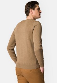 Brązowy sweter dzianinowy z okrągłym dekoltem, długimi rękawami i ribanowym pasem. Tkanina wydaje się miękka, z delikatną teksturą.