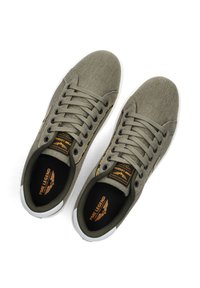 Baskets en toile vert olive avec semelles blanches en caoutchouc, bouts ronds et lacets plats. Elles comportent des étiquettes de logo et une surface texturée sur le dessus.