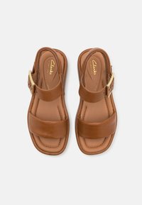 Brown leather sandals featuring two wide straps, an adjustable buckle, and a cushioned footbed for comfort. Simple rectangular shape.