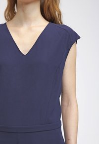 Tmavě modrý overal s výstřihem do V a krátkými rukávy, hladká tkanina, přiléhavý pas a jemné lesknutí, vytvářející elegantní siluetu.