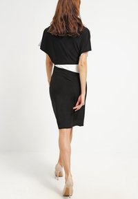 Svart klänning med en figurnära silhuett, mjukt tyg och vit midjebandaccent, med korta ärmar och knälång längd.