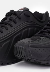Black athletic shoes feature a sleek design with perforated accents, textured fabric, and a durable rubber sole. Laces are integrated into the design.