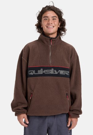 Bruine fleece pullover met een hoge kraag, halve rits, rode accenten en een zwarte band met het "Quiksilver" logo, inclusief zijzakken.